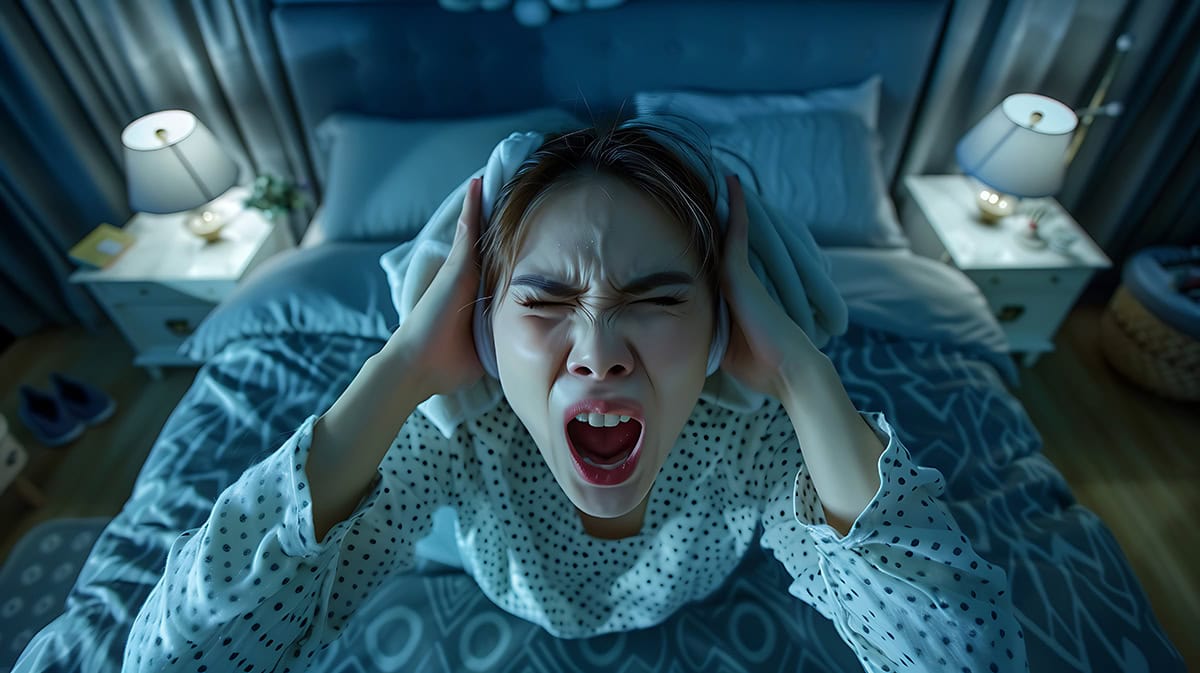 mujer de pies encima de una cama con cara irritada y la boca abierta por no poder dormir