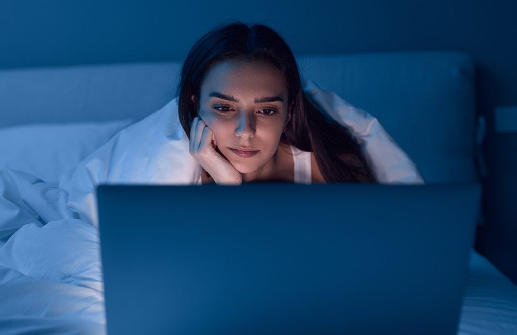 mujer dentro de una cama viendo un portátil